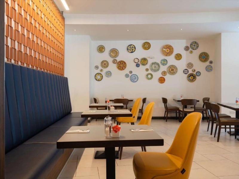 Área de comedor moderna con sillas amarillas, bancos azul oscuro y objetos decorativos en la pared.