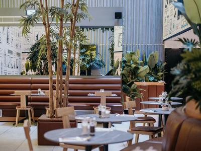 Ristorante d'hotel moderno con tavoli rotondi, panche imbottite e piante verdi.