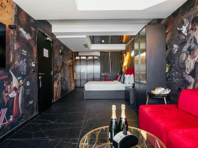 Camera d'hotel moderna con letto grande, divano rosso, murales elaborati e champagne sul tavolo.