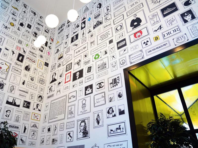 Parete dell'hotel coperta da numerose foto in bianco e nero di ritratti in varie cornici con piante davanti.