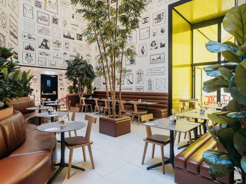 Caffè moderno con sedie in legno e pelle, grande vetrata gialla e piante.