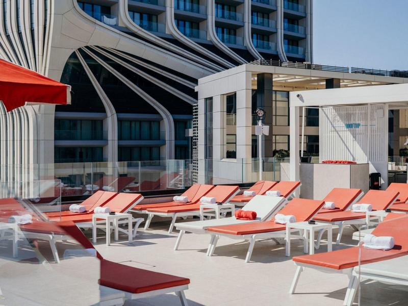 Terrazza sul tetto con sedie a sdraio rosse e edifici bianchi moderni sullo sfondo.