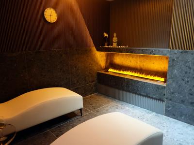 Moderne Wellness-Lounge mit zwei weißen Liegen und beleuchtetem Kamin in dunklem Raum.
