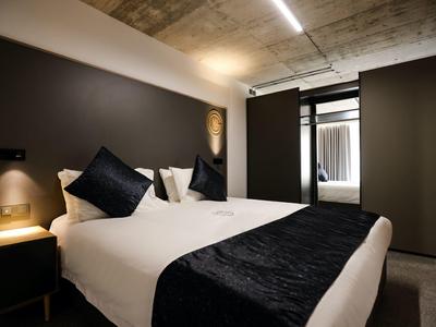 Nowoczesny pokój hotelowy z łóżkiem podwójnym, czarnymi poduszkami i współczesnym oświetleniem.