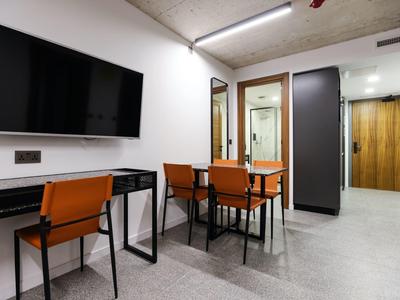 Nowoczesne miejsce do pracy w pokoju hotelowym z biurkiem, telewizorem i pomarańczowymi krzesłami.