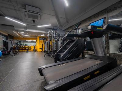 Moderner Fitnessraum mit Laufbändern, Gewichten und gelber Wand im Hintergrund.