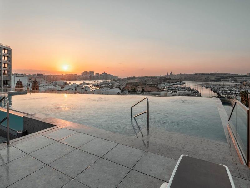 Basen nieskończoności na tarasie na dachu z widokiem na miasto i zachód słońca.