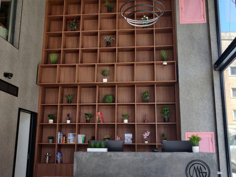 Nowoczesna recepcja hotelowa z betonowym i drewnianym wystrojem, dużymi oknami i dekoracyjnymi półkami.