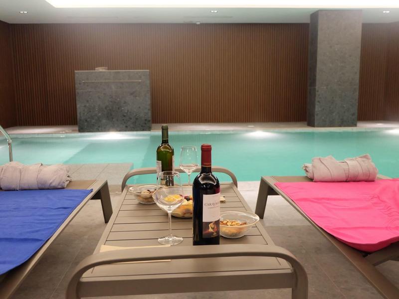 Relaksująca strefa basenu krytego z leżakami, winem i przekąskami dla gości.