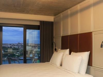 Modern hotel room with large bed, bedside lamps, and city view through sliding glass door.