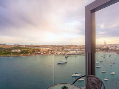 Blick von einem Balkon mit Glasgeländer auf einen Hafen mit Booten bei Sonnenuntergang.