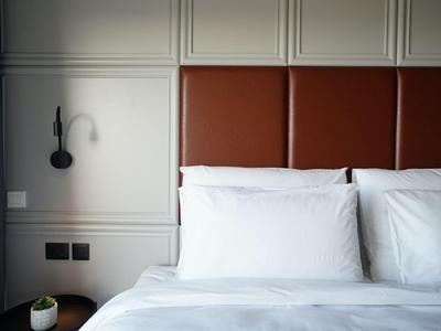 Minimalist hotel room with white bedding, brown leather headboard, and black wall lamp.