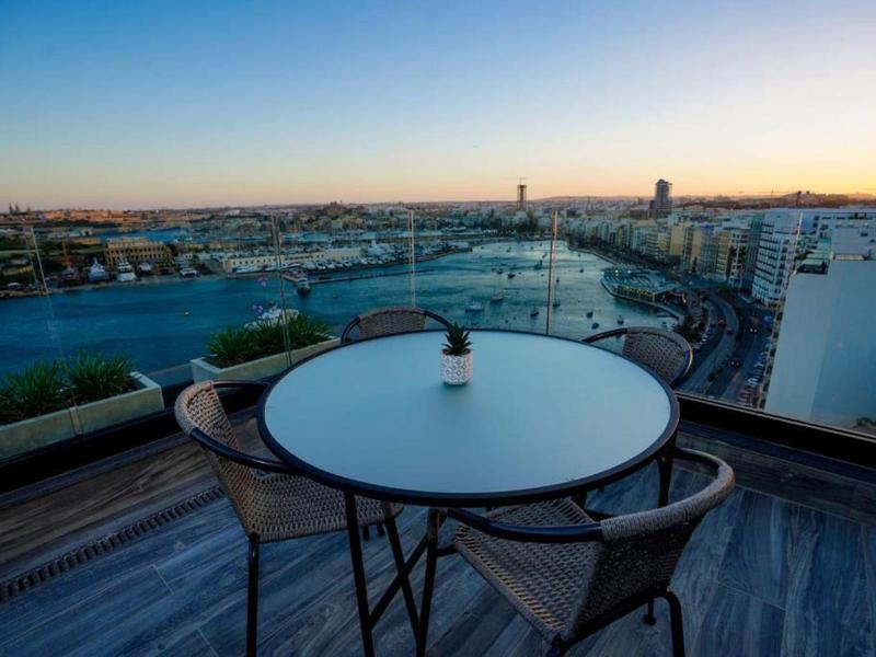 Outdoor seating with round table on hotel balcony overlooking city river at sunset.