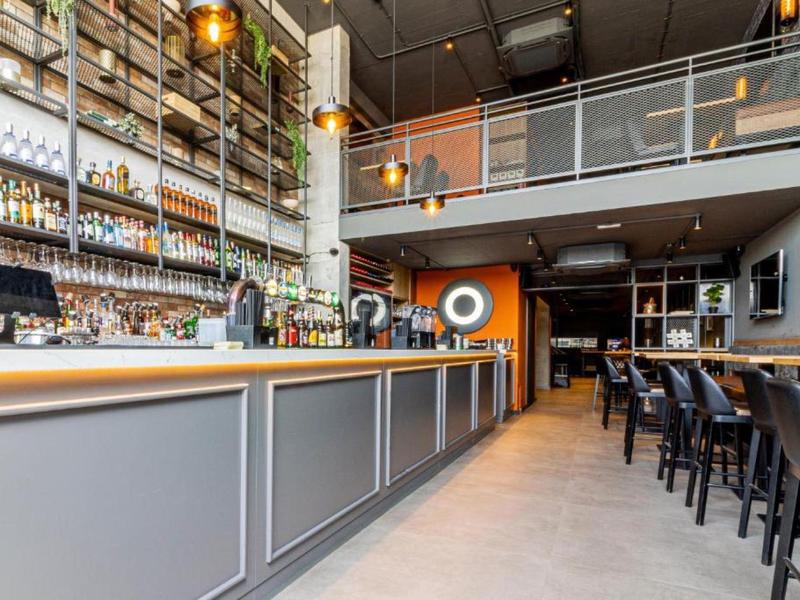 Spacious hotel bar with modern seating, high shelves filled with bottles, and a mezzanine level.