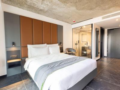 Modernes Hotelzimmer mit Doppelbett, gepolstertem Kopfteil, grauem Boden und offenem Badbereich.