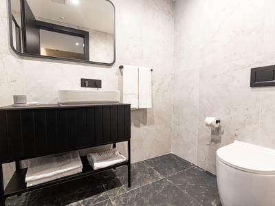 Moderner, minimalistischer Badbereich mit schwarzem Waschbeckenunterschrank, weißer Toilette und grauen Fliesen.