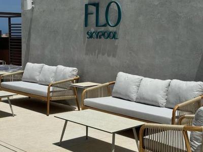 Moderne Lounge mit grauem Betonwand, zwei Holzsesseln, Sofas mit weißen Kissen und zwei Tischen.