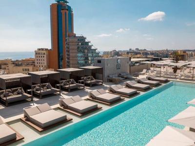 Dachterrasse mit großem Pool, Liegen und moderner Stadtkulisse im Hintergrund.