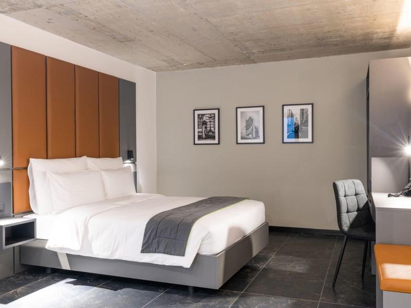 Modernes Schlafzimmer mit großem Bett, orangefarbenem Kopfteil, Schreibtisch und drei Bildern an der Wand.