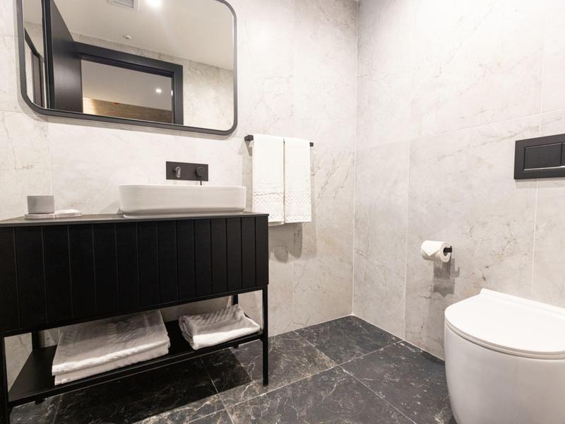 Moderner, minimalistischer Badbereich mit schwarzem Waschbeckenunterschrank, weißer Toilette und grauen Fliesen.