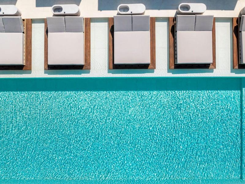 Vogelperspektive auf blauen Pool mit fünf weißen Liegen und Sonnenliegen am Rand.