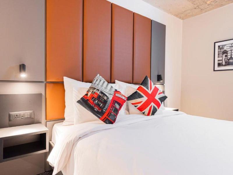 Modernes Schlafzimmer mit großem weißen Bett, orangefarbenem Kopfteil und dekorativen Kissen.