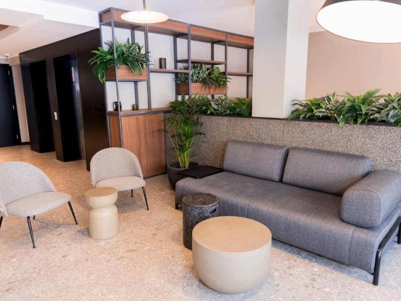 Moderner Wartebereich mit grauem Sofa, zwei Sesseln, Pflanzen und warmem Deckenlicht.