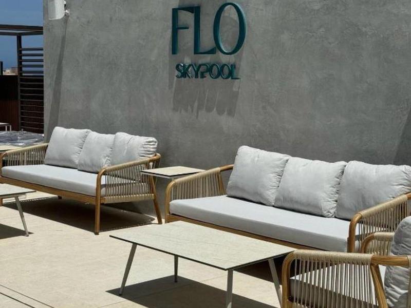 Moderne Lounge mit grauem Betonwand, zwei Holzsesseln, Sofas mit weißen Kissen und zwei Tischen.