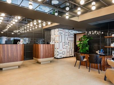 Moderner Hotel-Lobbybereich mit Holzmöbeln, geometrischem Wandmuster und Beleuchtung an der Decke.