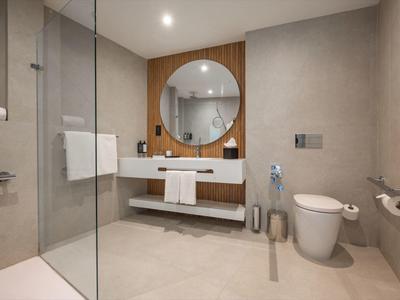 Modernes Badezimmer mit runder Spiegel, Waschtisch, Toilette und Dusche mit Glaswand.