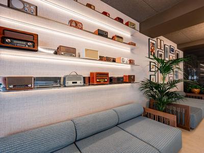 Modern eingerichteter Wartebereich mit grauem Sofa, Pflanzen und Regalen mit Retro-Radios.