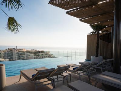 Dachterrasse mit Infinity-Pool, Liegestühlen und Ausblick auf die Stadt und das Meer.