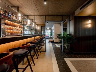 Moderner Hotelbar-Bereich mit Holztheke, hohen Stühlen und stilvoller Beleuchtung.