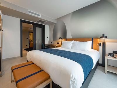 Modernes Hotelzimmer mit großem Bett, Sitzbank und minimalistischem Dekor.