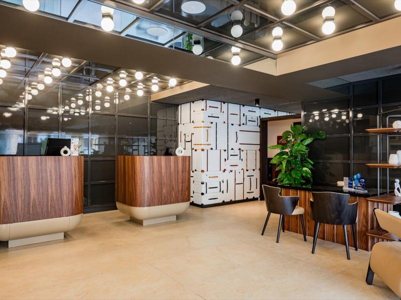 Moderner Hotel-Lobbybereich mit Holzmöbeln, geometrischem Wandmuster und Beleuchtung an der Decke.