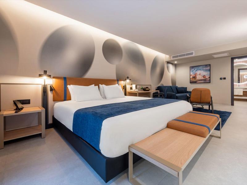 Modernes Hotelzimmer mit großem Bett, Sitzbereich und stilvoller Wandgestaltung.