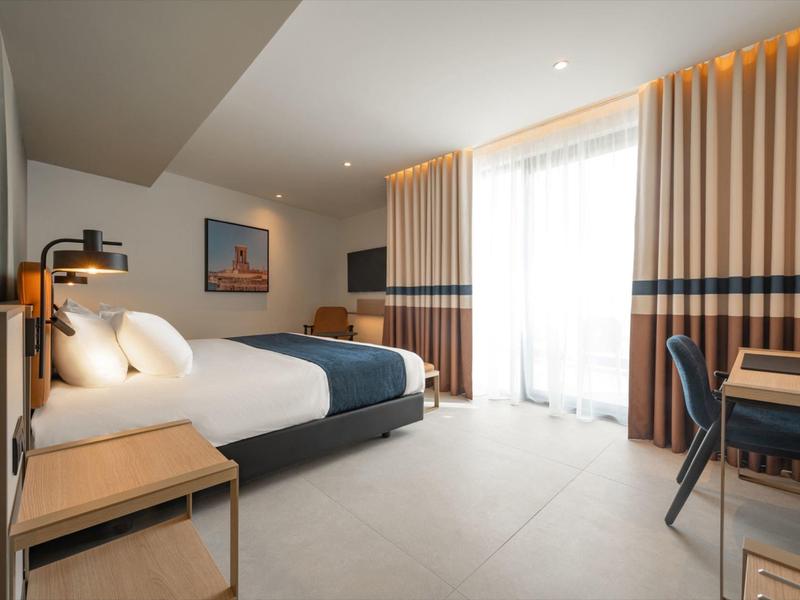 Modernes Hotelzimmer mit Doppelbett, Stühlen und großem Fenster mit Vorhängen.