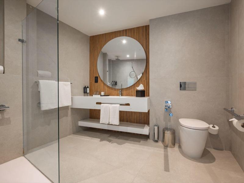 Modernes Badezimmer mit runder Spiegel, Waschtisch, Toilette und Dusche mit Glaswand.