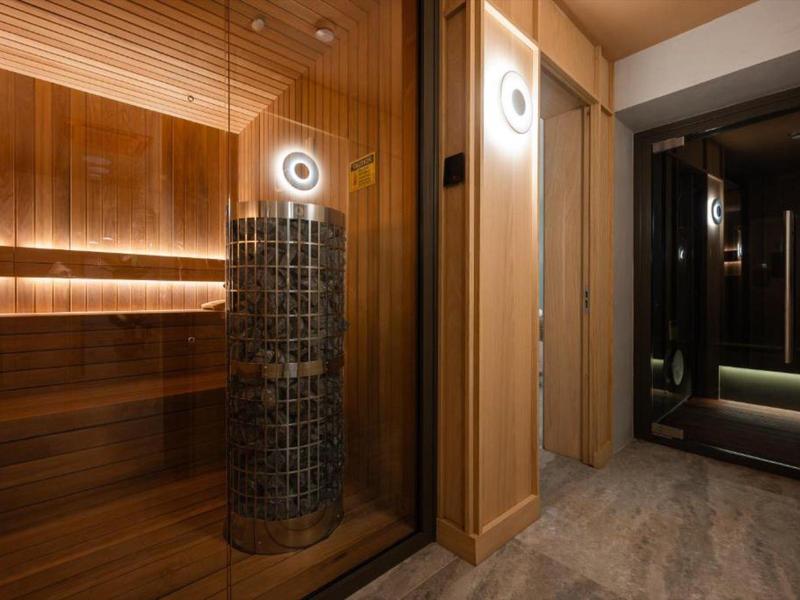 Moderner Saunaraum mit beleuchtetem Steinofen und Holzverkleidung neben Spiegel und Tür.