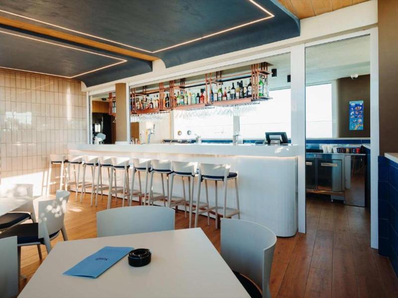 Moderner Hotelbarbereich mit hoher Theke und Barhockern, eleganter Ausstattung und Holzboden.