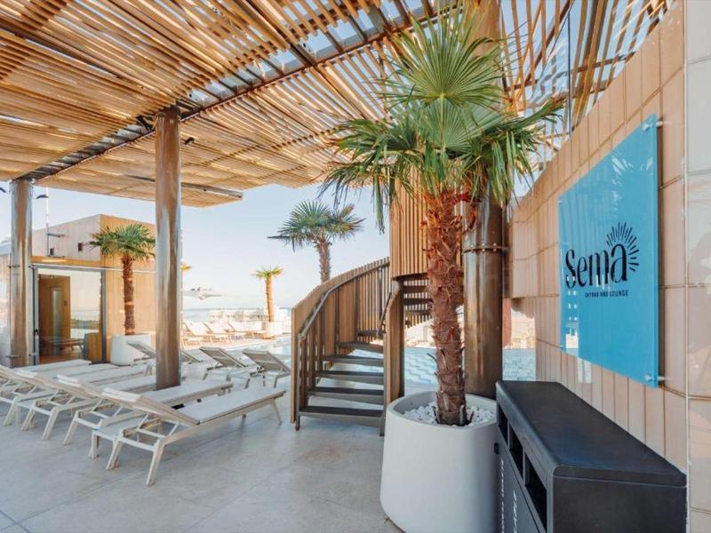 Überdachter Außenbereich mit Liegestühlen, Treppe und Palmen an einem sonnigen Ort.