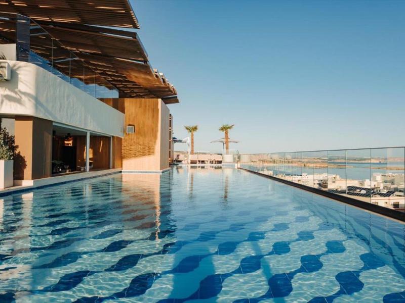 Moderner Infinity-Pool mit Meerblick auf der Dachterrasse eines Hotels bei klarem Himmel.