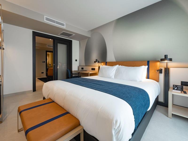 Modernes Hotelzimmer mit großem Bett, Ledersitzbank und hellen Wänden.