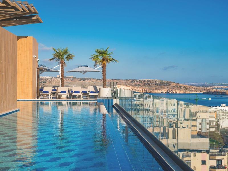 Infinity-Pool mit Blick auf die Küste und Sonnenschirme an einem sonnigen Tag.