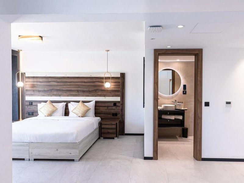 Modern hotel room with double bed, wooden headboard, and bathroom with round mirror.