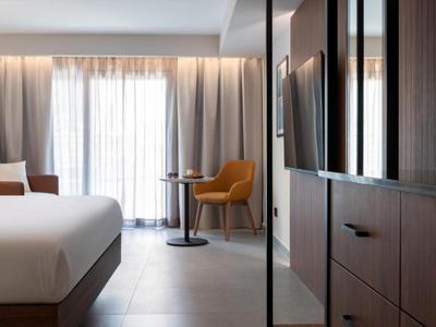 Habitación de hotel moderna con cama grande, sillón y ventana con cortinas.