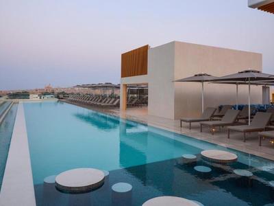 Moderner Hotelpool mit Liegestühlen und Blick auf das Meer bei Sonnenuntergang.