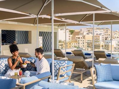 Pareja sentada en terraza en la azotea con sombrillas y vista a la ciudad en un día soleado.