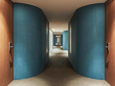 Pasillo moderno de hotel con paneles azules curvos y puertas de madera.