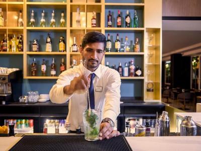 Barman preparando un cóctel en la barra con botellas al fondo.